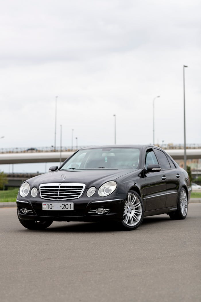 A stylish black Mercedes-Benz sedan parked on a roadside under a cloudy sky.